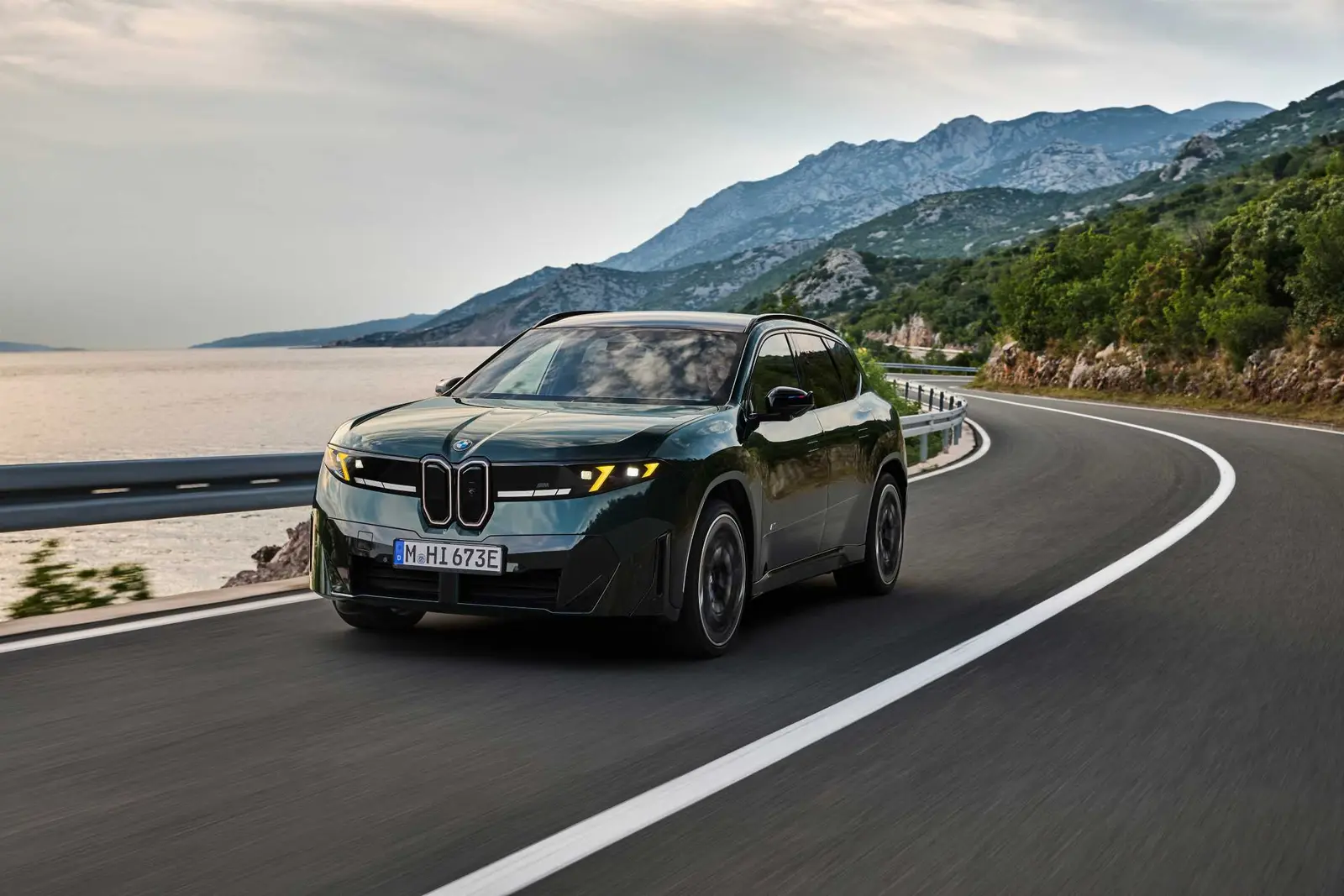 Dark green BMW iX3 M60 xDrive driving on a coastal mountain road